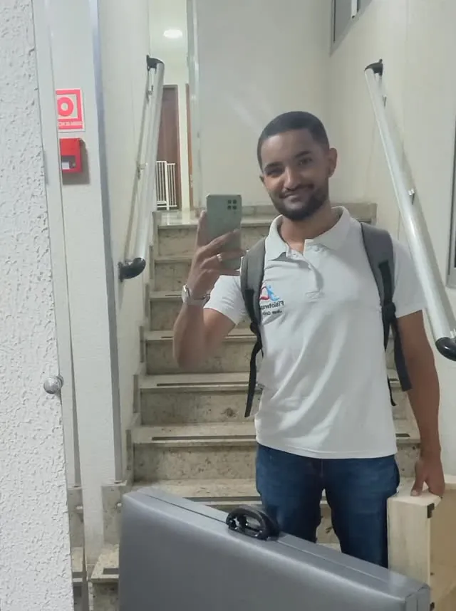 Jean Carlos subindo a escada de um prédio com a maca portátil para um atendimento de fisioterapia em casa