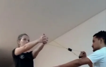 Jean Carlos orientando uma paciente em exercício com elástico na sala de casa, em Santo André